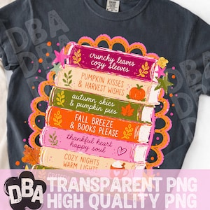 May include: A dark charcoal gray t-shirt featuring a graphic of a stack of colorful books. The book spines display text including crunchy leaves cozy sleeves, pumpkin kisses & harvest wishes, autumn skies & pumpkin pies, fall breeze & books please.