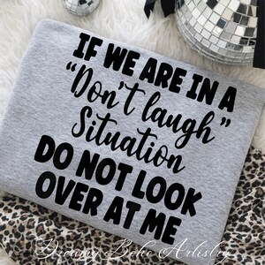 May include: A light gray sweatshirt with the text "IF WE ARE IN A 'Don't laugh' Situation DO NOT LOOK OVER AT ME" in black. The sweatshirt is folded on a leopard print fabric.