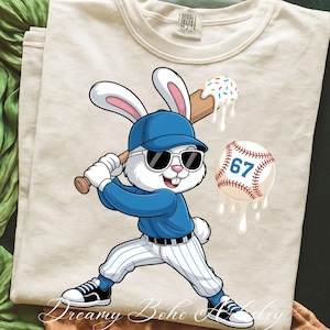 May include: Cream-colored t-shirt featuring a cartoon rabbit in a baseball uniform, wearing sunglasses and holding a bat. A baseball with the number 67 and a melting ice cream cone are also depicted. The shirt has the text "Dreamy Boho Artistry" at the bottom.