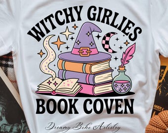 May include: White t-shirt with a colorful graphic design featuring a witch's hat, books, and the words "Witchy Girlies Book Coven." The design includes stars, a crescent moon, and a potion bottle with a feather quill.