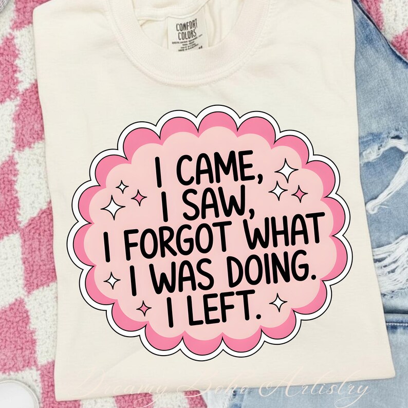 May include: Cream-colored t-shirt with a pink and white graphic that reads "I CAME, I SAW, I FORGOT WHAT I WAS DOING. I LEFT." The graphic has a scalloped edge and star accents. The shirt has a Comfort Colors tag.