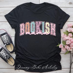 May include: Black t-shirt with the words "BOOKISH mama" in a floral design. The shirt is paired with black canvas sneakers and a bouquet of pink flowers. The words "Dreamy Boho Artistry" are written in cursive at the bottom.