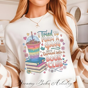 Puede incluir: Sudadera blanca con un diseño gráfico colorido que presenta una bebida de café helado de dibujos animados, libros y el texto "Intenté formar una pandilla, pero se convirtió en un club de lectura".