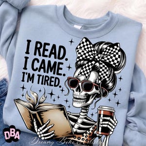 May include: Light blue sweatshirt with a graphic of a skeleton reading a book and holding a coffee cup. The skeleton wears sunglasses and a checkered bow. Text on the shirt reads: "I READ. I CAME. I'M TIRED."