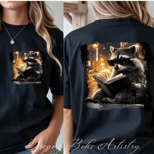May include: Black t-shirt featuring a raccoon wearing sunglasses and reading a book, set against a city street scene. The design is on the front and back of the shirt. The text "Dreamy Boho Artistry" is at the bottom of the shirt.