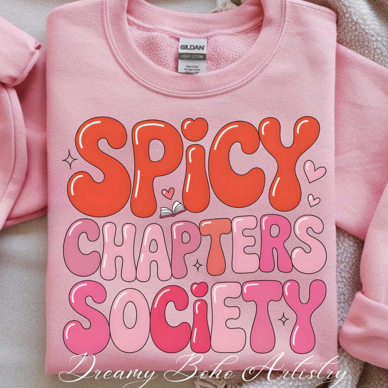 May include: Pale pink sweatshirt featuring the text "Spicy Chapters Society" in a retro font. The text is in shades of orange and pink, with heart and star accents. The brand tag is visible.