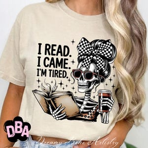 May include: Beige t-shirt with a skeleton graphic wearing sunglasses and a checkered bow, holding a book and a coffee cup. The text on the shirt reads "I READ. I CAME. I'M TIRED."