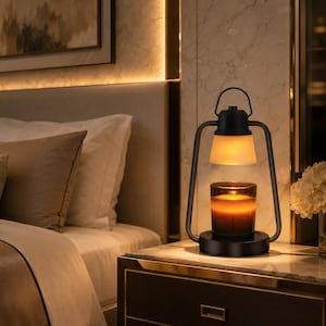 May include: A black metal candle warmer lamp with a lantern-style frame and a frosted glass shade. The lamp features a circular base holding a dark glass candle jar, emitting a warm, soft glow from the heating element positioned above the wax.