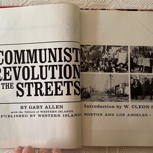 Puede incluir: Libro abierto con el t&iacute;tulo "COMMUNIST REVOLUTION IN THE STREETS" de Gary Allen. La portada presenta texto negro sobre fondo blanco, con fotos hist&oacute;ricas en blanco y negro. Publicado por Western Islands en 1967.