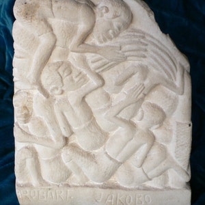 May include: A white stone sculpture of several figures in a reclining pose. The sculpture is signed "ROBART JAKOBO".