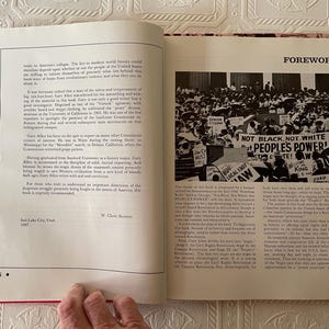 Puede incluir: Un libro abierto con encuadernaci&oacute;n roja, que muestra texto y una fotograf&iacute;a en blanco y negro de una multitud con carteles. El texto incluye la palabra "FOREWORD" y la frase "NOT BLACK, NOT WHITE, PEOPLE'S POWER!"