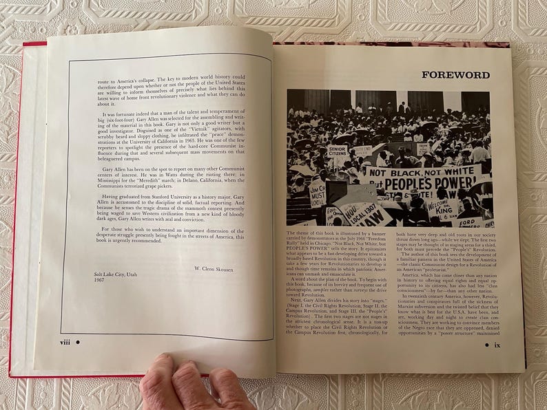 Puede incluir: Un libro abierto con encuadernaci&oacute;n roja, que muestra texto y una fotograf&iacute;a en blanco y negro de una multitud con carteles. El texto incluye la palabra "FOREWORD" y la frase "NOT BLACK, NOT WHITE, PEOPLE'S POWER!"