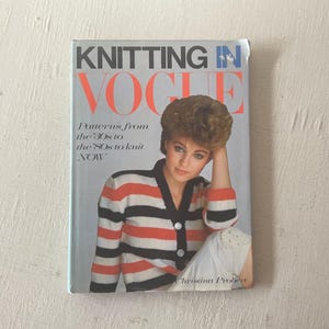 May include: A book titled "Knitting in Vogue" with a woman on the cover wearing a striped red and black sweater. The book cover text says "Patterns from the '30s to the '80s to knit NOW".