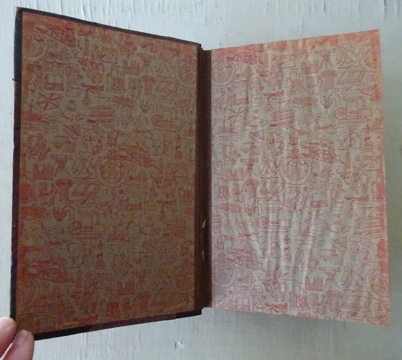 May include: An open book with a brown leather cover and red patterned endpapers. The endpapers feature a repeating design of various small objects, including tools, buildings, and plants.