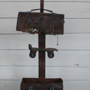 May include: A rusty metal lamp with a unique design. The lampshade is made of a rusty metal sheet with holes. The base of the lamp is a rusty metal box with two metal handles. The lamp has a roller skate attached to the base.