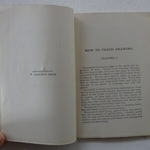 Peut inclure: Un livre vintage intitul&eacute; "How to Teach Drawing" avec la date de copyright 1914 par W. Hazleton Smith. Le livre est ouvert au premier chapitre, qui traite de l'importance d'apprendre aux enfants &agrave; observer et &agrave; comprendre la forme avant de dessiner.