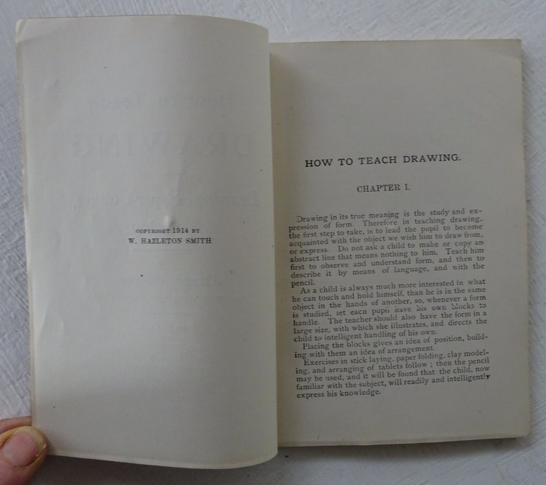Peut inclure: Un livre vintage intitul&eacute; "How to Teach Drawing" avec la date de copyright 1914 par W. Hazleton Smith. Le livre est ouvert au premier chapitre, qui traite de l'importance d'apprendre aux enfants &agrave; observer et &agrave; comprendre la forme avant de dessiner.