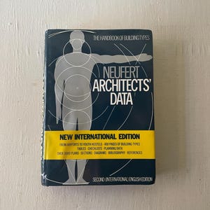 May include: A hardcover book titled "NEUFERT ARCHITECTS' DATA" with a dark blue cover and yellow banner. The book features a stylized human figure illustration and text detailing building types, plans, and references. The edition is labeled as "NEW INTERNATIONAL EDITION".
