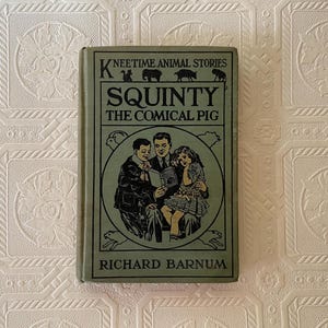 May include: A vintage book titled "Squinty the Comical Pig" by Richard Barnum. The cover is green with black text and illustrations, including a family reading a book. The book is part of the "Kneetime Animal Stories" series.