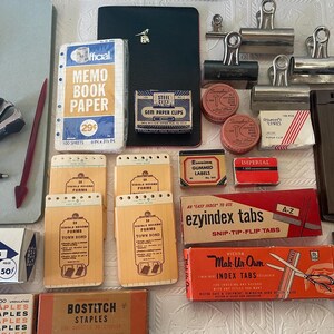 May include: An assortment of vintage office supplies, including a ledger, memo book paper, staplers, paper clips, index tabs, and blank cards. The items are in various colors, with visible text on the packaging.