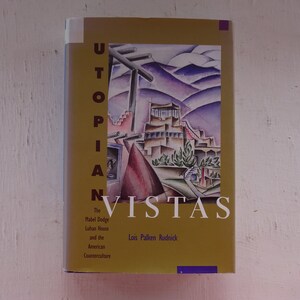 May include: A book cover with a yellow background and the title "Utopian Vistas: The Mabel Dodge Luhan House and the American Counterculture" by Lois Palken Rudnick. The cover features a colorful illustration of a building with a mountain range in the background.