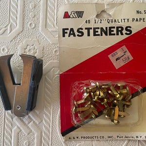 May include: An image of office supplies. A package of brass fasteners and a black and silver staple remover are displayed. The fastener package has red and white packaging with the text "FASTENERS". The staple remover is made of metal and black plastic.