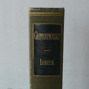 May include: A green book with gold lettering on the spine. The title is "Geomorphology" by Lobeck.