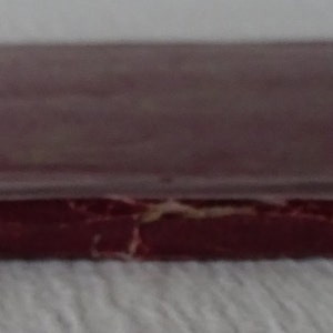 Peut inclure: Un livre reli&eacute; en bordeaux avec une couverture us&eacute;e et une colonne vert&eacute;brale visible.
