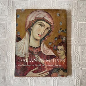 May include: A hardcover book titled "Italian Primitives" featuring panel paintings from the twelfth and thirteenth centuries. The cover displays a religious painting with a woman in a head covering and a child. The book has a worn, vintage appearance.