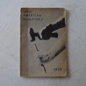 May include: A vintage book cover with a black and white photo of a hand holding a hammer and chisel. The book title is "United American Sculptors" and the year "1939" is printed on the bottom right corner.