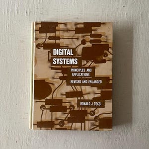 May include: A brown book titled "Digital Systems: Principles and Applications, Revised and Enlarged" by Ronald J. Tocci. The cover features a circuit board design.