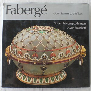 May include: A book titled "Fabergé: Court Jeweler to the Tsars" by G. von Habsburg-Lothringen and A. von Solodkoff. The cover features a detailed image of a Fabergé egg, a white egg with a gold and jeweled latticework design.