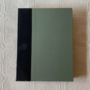 May include: A hardcover book with a black spine and a muted green cover. The book is rectangular and appears to be closed. The cover is a solid color, and the spine is a darker shade of black.