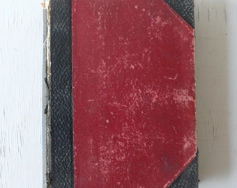 Può includere: Un libro vintage rosso rilegato con rivestimento in pelle nera e una copertina usurata e testurizzata.