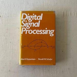 May include: A yellow book titled "Digital Signal Processing" by Alan V. Oppenheim and Ronald W. Schafer. The cover features a diagram with arrows and the text "z-1" and "x(n)" and "y(n)".