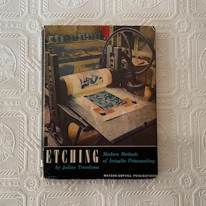May include: A vintage book titled "Etching" by Julian Trevelyan, showcasing modern methods of intaglio printmaking. The cover features a detailed illustration of a printing press in a workshop setting, with the title in bold white letters.