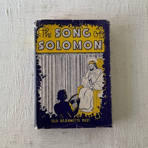 May include: A vintage book titled "The Song of Solomon" by Ella Arjennete Rust. The cover features a blue background with a yellow title and a black and white illustration of a man sitting on a throne with a woman kneeling before him.