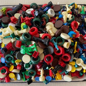 May include: A collection of colorful game pieces in a white metal tray. The pieces include pawns, kings, queens, and other game pieces in various colors, including red, blue, green, yellow, and black.