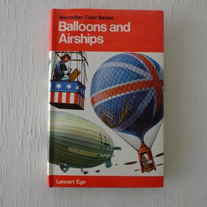 May include: A red book with the title "Balloons and Airships" from the Macmillan Color Series. The cover features illustrations of a hot air balloon with a Union Jack design, a blimp, and a smaller hot air balloon with an American flag design.