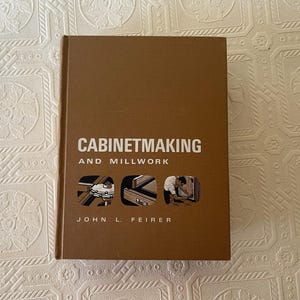 May include: A brown hardcover book titled Cabinetmaking and Millwork by John L. Feirer. The front cover features white text and three small circular illustrations depicting woodworking tools, a drawer assembly, and a person working on cabinetry.