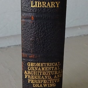 May include: A black leather-bound book with gold lettering. The title is "I.C.S. Reference Library Geometrical Ornamental Architectural Freehand and Perspective Drawing". The book is from International Correspondence Schools.
