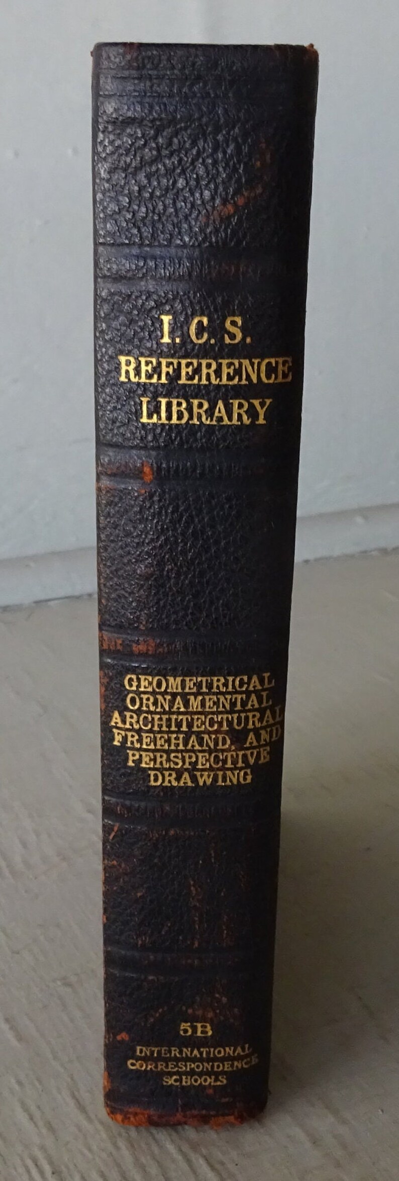 May include: A black leather-bound book with gold lettering. The title is "I.C.S. Reference Library Geometrical Ornamental Architectural Freehand and Perspective Drawing". The book is from International Correspondence Schools.