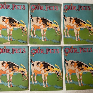 May include: Six vintage children's books with a blue cover and the title "OUR PETS" printed in pink. Each book features an illustration of a goat with brown and white markings on a green background.
