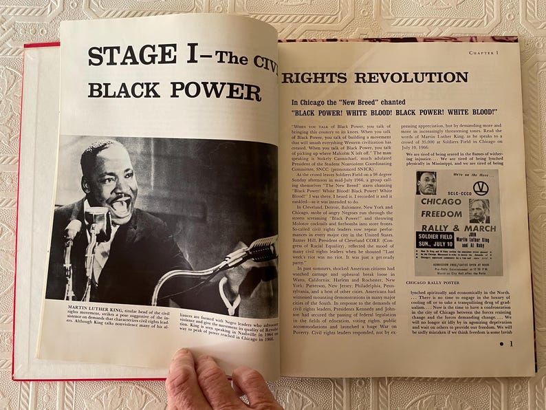 Puede incluir: Un libro abierto con lomo rojo, con una fotograf&iacute;a en blanco y negro de Martin Luther King Jr. hablando. El texto dice "STAGE I - The Civil Rights Revolution" y "BLACK POWER". Tambi&eacute;n es visible un cartel de una manifestaci&oacute;n de Chicago Freedom.
