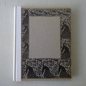 May include: A white book with a black and white peacock design on the cover. The design is a border around a blank space in the center of the cover.