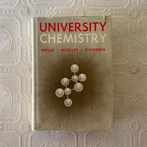 May include: A white ceramic mug with a black handle and the text "But First, Coffee" in a black, handwritten-style font. The mug is on a white surface.