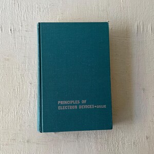 May include: A teal-colored hardcover book titled "PRINCIPLES OF ELECTRON DEVICES" by Gillie. The book has a simple, clean design with the title in silver lettering. The book is set against a white, textured background.