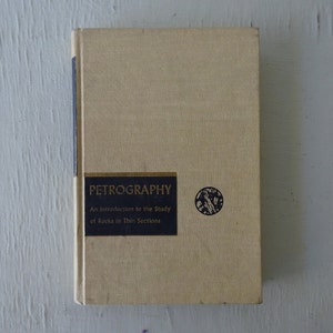 May include: A beige book with the title "Petrography: An Introduction to the Study of Rocks in Thin Sections" printed in gold lettering on a black background.