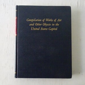 May include: A dark blue hardcover book with gold lettering on the spine and front cover. The title is "Compilation of Works of Art and Other Objects in the United States Capitol".