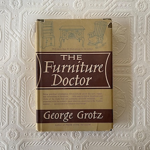 May include: A vintage book titled "The Furniture Doctor" by George Grotz. The cover is tan and brown with illustrations of furniture. The book provides practical information on furniture care, repair, and refinishing.